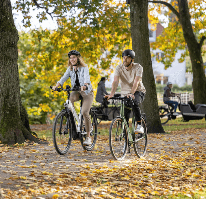 Bestelle-ein-Bike-online Zwei RADWELT Mitarbeiter fahren mit dem Fahrrad durch einen Park in Coesfeld.